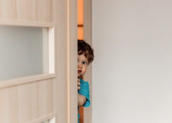 little kid hiding behind the door playing hide and seek