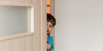 little kid hiding behind the door playing hide and seek