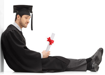 Sad graduate student with a diploma sitting on the floor and leaning on a wall isolated on white background