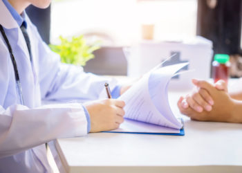 Doctor man consulting patient while filling up an application form at the desk in hospital. Medicine and health care concept