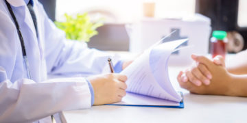 Doctor man consulting patient while filling up an application form at the desk in hospital. Medicine and health care concept