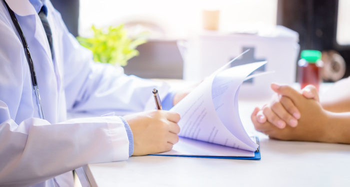 Doctor man consulting patient while filling up an application form at the desk in hospital. Medicine and health care concept