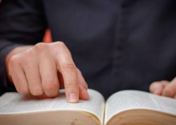 Hands folded in prayer on a Holy Bible in church concept for faith, spirtuality and religion