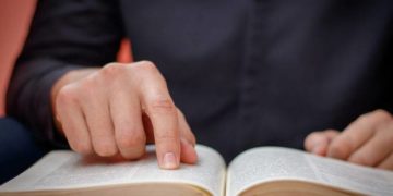 Hands folded in prayer on a Holy Bible in church concept for faith, spirtuality and religion